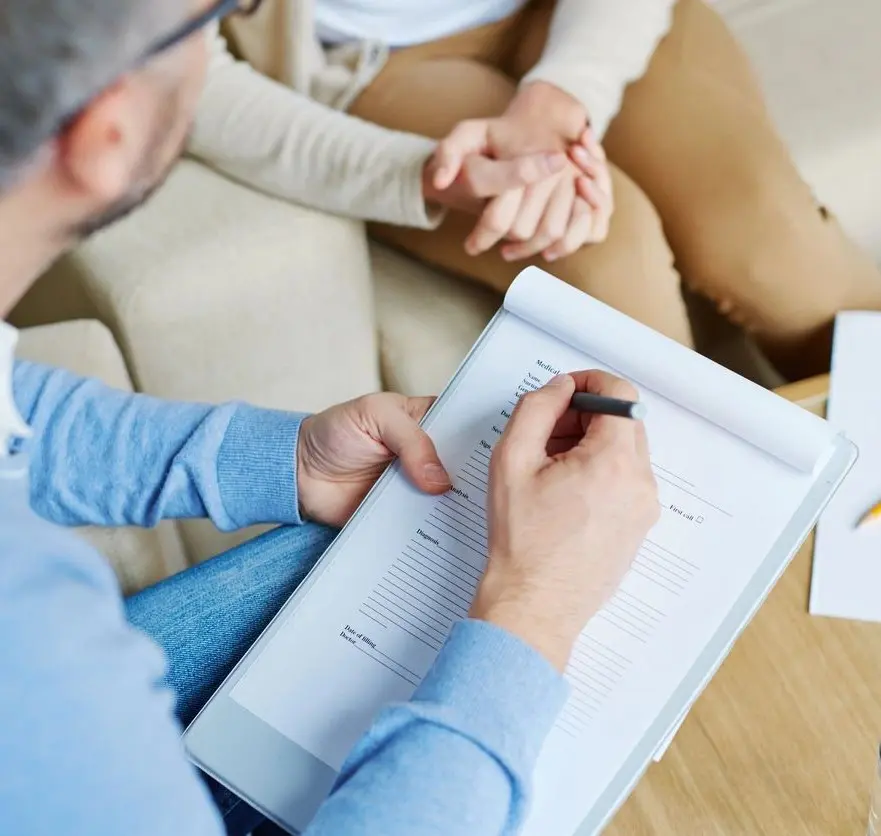 A man writing on paper while sitting next to another person.