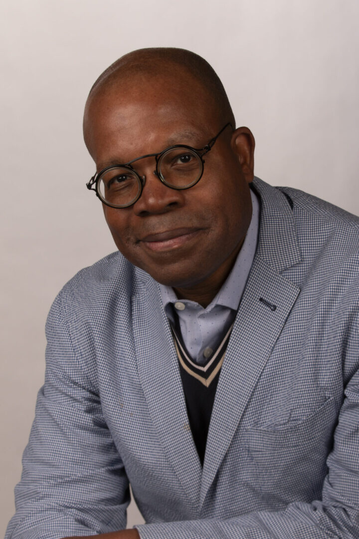 A man in glasses and a jacket is sitting